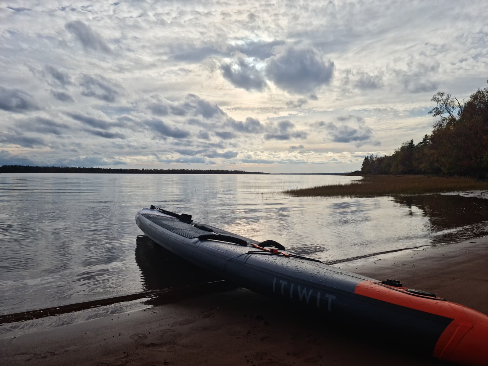 An inflatable kayak drawn up on a bright, calm lakeshore
